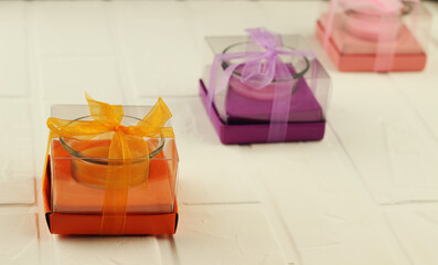 Three scented candles in the form of a glass beaker in gift wrap of pink, purple and orange colors....