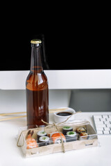 Assorted sushi and rolls near the computer. Eating at the workplace. Relax at home with a bottle of beer.