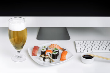 Assorted sushi and rolls near the computer. Eating at the workplace. Relax at home with a glass of beer.
