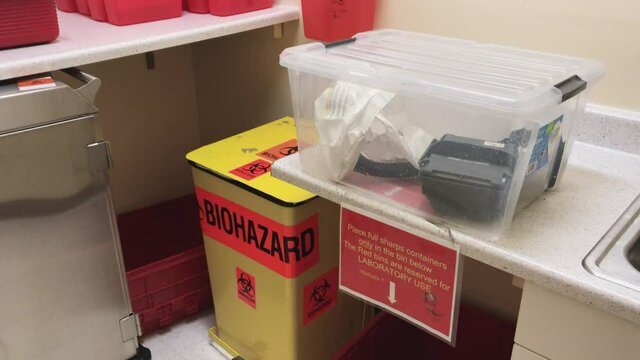 Biohazard medical waste and sharps containers in hospital clinic room.