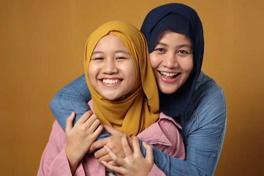 People And Family Concept - Happy Smiling Asian Muslim Mother Hugging Daughter Against Yellow Background