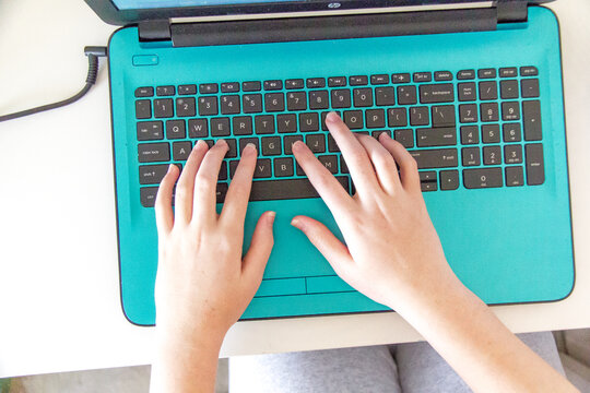 Girls hands on a teal laptop keyboard during online learning at home