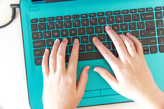 Girl typing on a teal keyboard of a laptop during online learning at home