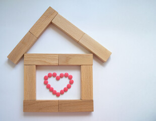 House of wooden blocks on a white background with a pink heart made of pills inside. The pink tablets are arranged in the shape of a heart. Vitamins for the heart.
