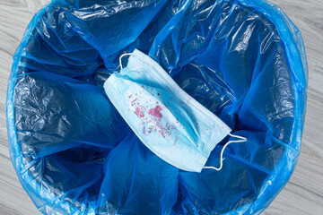 in the bin there is a bloodied medical mask with a blue plastic bag. vertical orientation,...