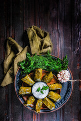 Traditional Georgian and Greek dolma in grape leaves on a wooden table with sour cream sauce and herbs. Copy space