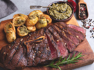 Sliced juicy grilled steak medium rare beef on the bone with roasted new potatoes sauce pesto