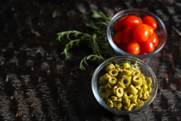 Fresh cherry tomatoes with sliced olives and a sprig of rosemary on a black wooden table