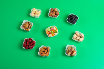 A serving of assorted candied fruit, dried cherries, almonds, raisins, walnuts and hazelnuts in paper muffin cups on a green background.