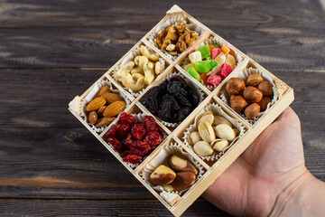 Assorted dried fruits and nuts in a wooden box isolated on a dark wood background. Raisins, candied fruits, cherries, Brazil nuts, hazelnuts, walnuts, almonds, cashews, pistachios.