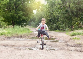 5 years boy is riding a bicycle through puddles in village in summer