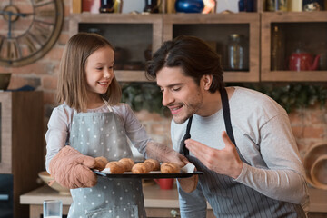 Cute little girl holding tray with fresh croissants, happy dad enjoying smell