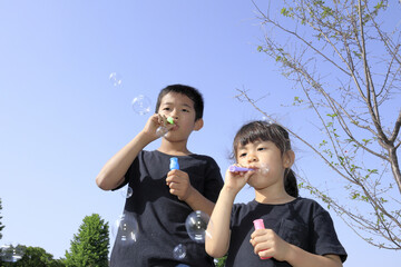 Naklejka premium シャボン玉で遊ぶ兄妹(10歳と5歳)と青空