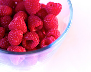 ripe fresh red raspberries in a glass plate on a white background