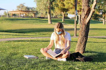 A student wearing a face mask studying outside.