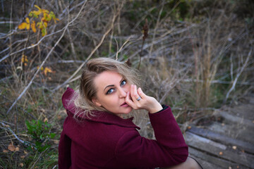 A girl in a purple coat looks directly at the camera. Portrait of a pensive lady on a wooden staircase.