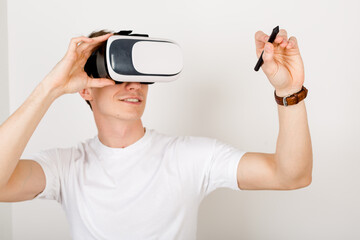 Male using virtual reality headset interacts with augmented things orienting in three dimensional space while sitting on his desk with keyboard and laptop on white background.