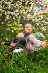 An elderly woman and a child. Grandma and grandson look at soap bubbles. Family in nature. Spring Park. Happiness. The elderly and the young.