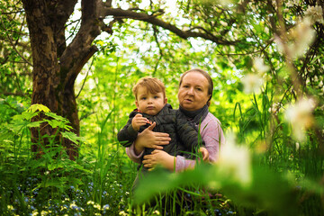 Grandma outdoors with a child smiling. Different generations. An elderly woman with her grandson in an Apple orchard. Spring Park.