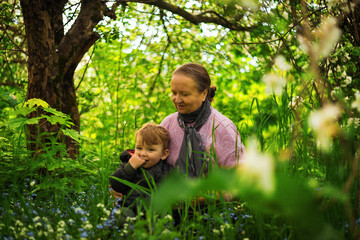 Grandma outdoors with a child smiling. Different generations. An elderly woman with her grandson in an Apple orchard. Spring Park.