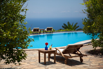 Summer and vacation concept. A glass of cocktail and colorful flowers. Sunbed, swimming pool and a wonderful sea view