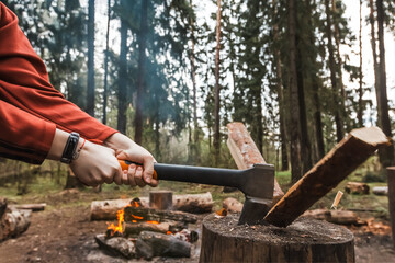 Female strong hands chop firewood with axe for bonfire. Powerful ax blow. Survival on camping trip....