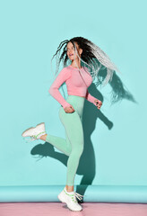 Young sport slim woman with modern hairstyle in sportswear and sneakers running jumping working out over pastel blue background