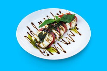 Caprese salad with tomatoes, mozzarella and pesto sauce isolated on blue background