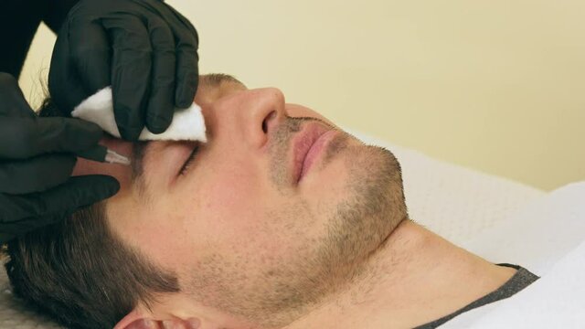 Close up of cosmetologist making permanent makeup. Microblading procedure. High quality close-up 4k slow motion video of a man laying on a couch during the esthetician brow microblading treatment.