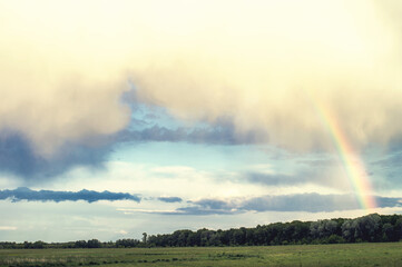Fluffy clouds and bright rainbow over the forest. Landscape of spring forested valley and beautiful cloudy sky