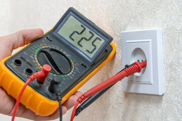 Electrician checks the voltage of the outlet using a digital multimeter, close-up