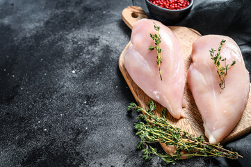 Raw chicken breast fillet on a chopping Board with herbs and spices. Black background. Top view. Copy space - obrazy, fototapety, plakaty