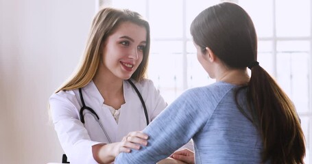 Young compassionate female doctor supporting woman at checkup meeting. Kind therapist sitting at table, encouraging millennial patient, having trustful conversation, reassuring client at clinic.