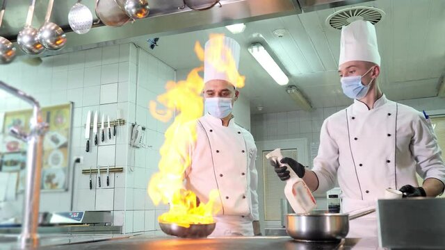 Chefs in protective masks and gloves prepare food in the kitchen of a restaurant or hotel