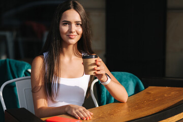 Attractive girl drink coffee on the terrace. Beautiful brunette resting during a break. Social distance