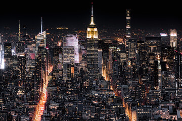 Aerial view of New York City at night with illuminated avenues converging towards midtown.