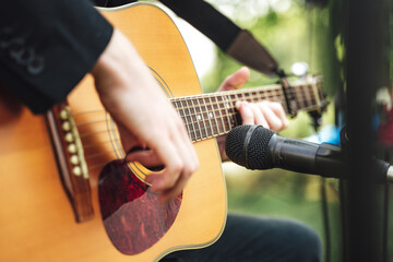 Man playing guitar. Closeup of male hands playing acoustic guitar. Outdoor background.