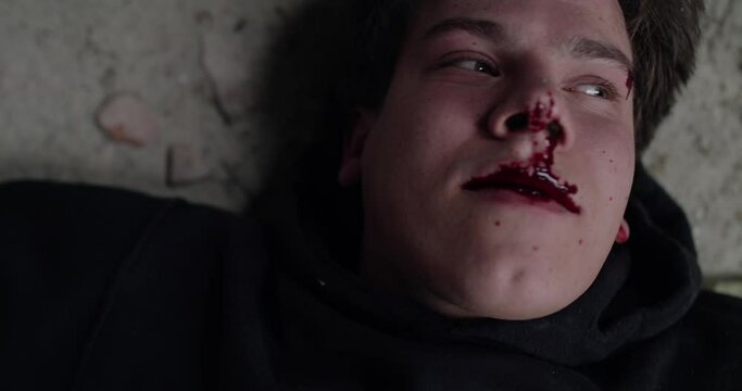 Close portrait of a wounded, bloodied man lies on a floor, coughs and suffocates