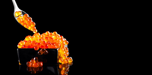 Red Caviar in a spoon. Caviar in bowl over black background. Close-up salmon caviar. Delicatessen. Gourmet food. Texture of caviar. Seafood isolated on black