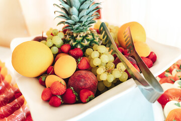Bowl with fresh fruit. Strawberries, grapes, pineapple, apple and citrus fruits on buffet table. Celebration, party, birthday or wedding concept.