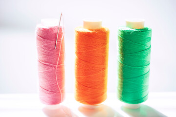 Three spools of thread and a needle on a white bright table, side view