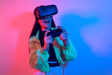 Laughing smiling surprise girl in neon with VR glasses holds a gamepad in her hands and plays games. Virtual world, technology.