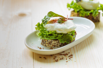 sandwich on grain bread with poached egg and green salad on a light background with space