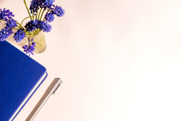 Blue flowers are on the white table and diary with pen top view