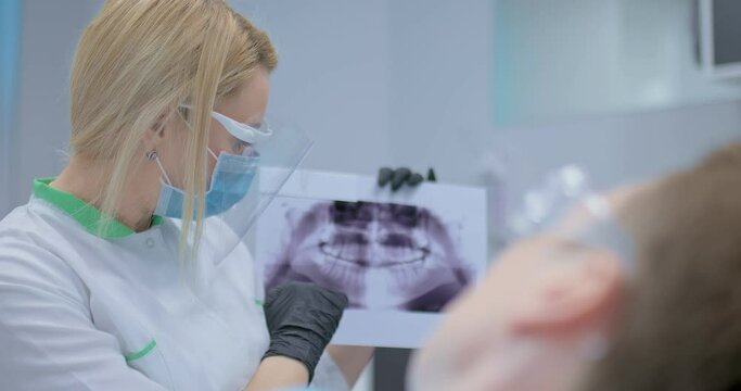 Orthodontist shows the patient an x-ray and explains the cause of the tooth disease. X-ray picture. Orthodontist consultation in a modern dental clinic.