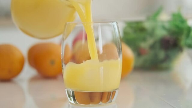 Glass of fresh orange juice. Woman pouring orange juice from glass jar into glass. Organic vitamin drink. Close-up in 4K, UHD