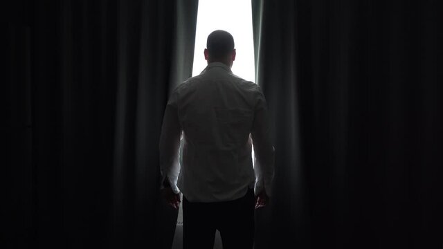Businessman in the morning at home, in unbuttoned shirt opens curtains and looks in window. Curtains swing open with the help of young bald guy.
