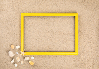 Fototapeta premium Yellow photo frame. Beach sand shells background.
