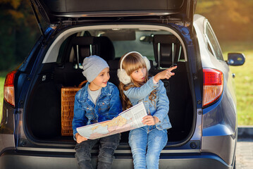 Agreeable boy and girl are looking at the road map while sitting in the auto's trunk and discussing the move direction. Family vacation trip by car.