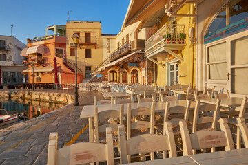 empty tables and chairs at the dock of the historic harbor of rethymno in the golden morning sun, fish restaurant at the quay